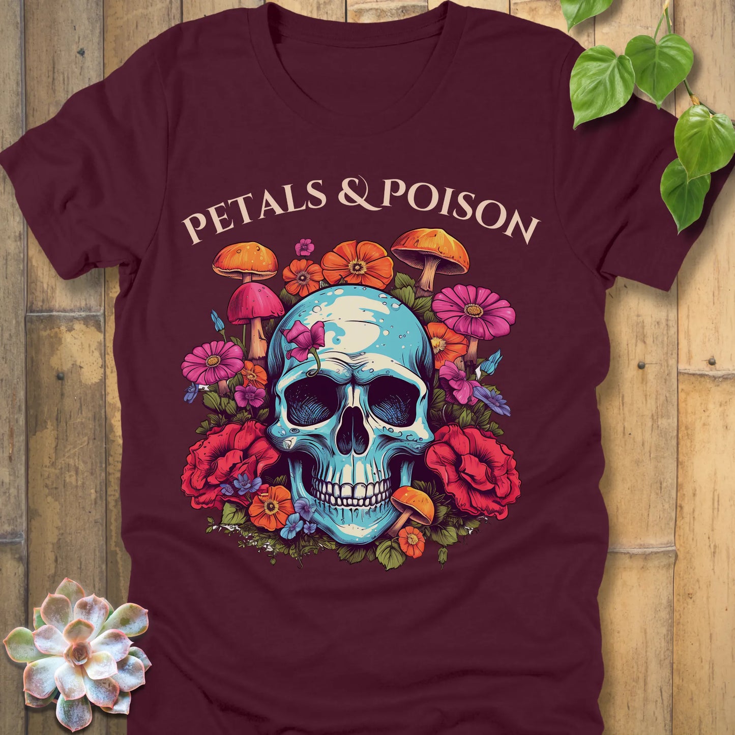 Maroon t-shirt featuring the design Petals & Poison printed in bold letters and a flowers, mushroom and skull