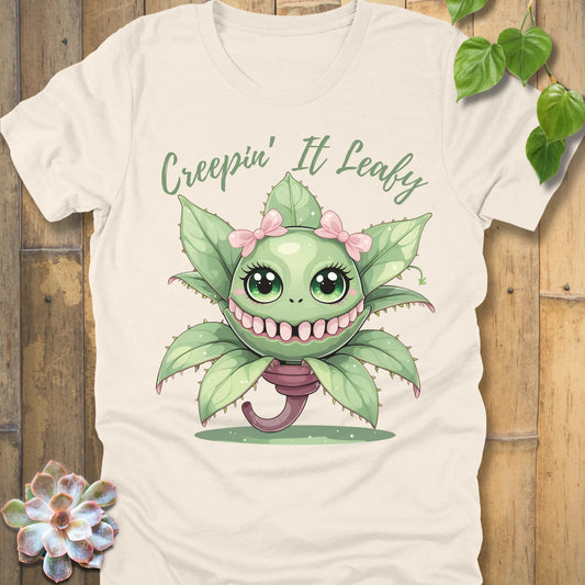 Natural t-shirt featuring the design Creepin' It Leafy printed in green letters and a happy plant
