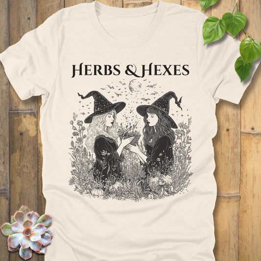 Natural t-shirt featuring the design Herbs & Hexes in black letters, printed with two witches