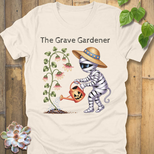 Natural t-shirt featuring the design The Grave Gardener printed in bold black letters and a ghost watering the plant